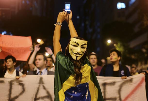 A demonstrator wearing a Guy Fawkes mask takes photos on her mobile phone during a protest in central Rio de Janeiro